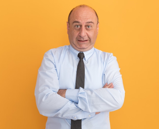 Hombre de mediana edad preocupado vestido con camiseta blanca con corbata cruzando las manos aisladas en la pared naranja