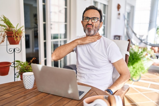 Foto gratuita hombre de mediana edad que usa computadora portátil en casa cortando la garganta con la mano como cuchillo, amenaza la agresión con violencia furiosa