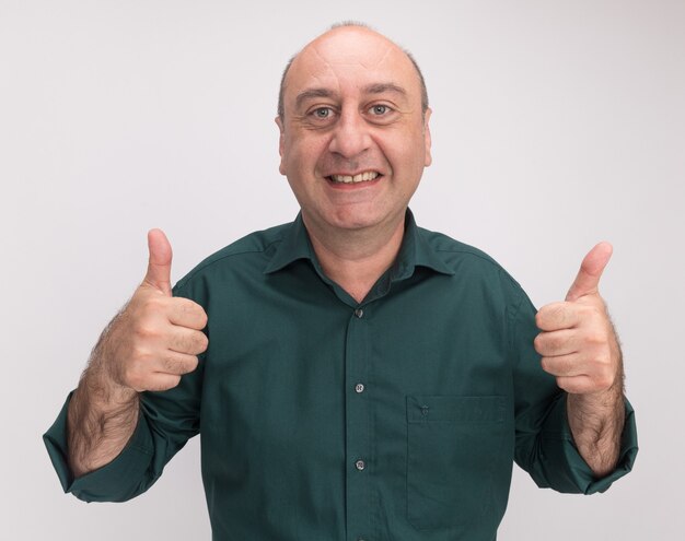 Hombre de mediana edad sonriente con camiseta verde que muestra los pulgares para arriba aislado en la pared blanca