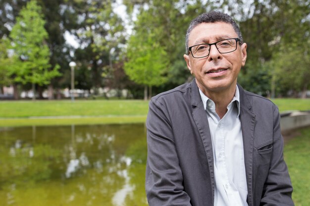 Hombre de mediana edad sonriente que presenta en la cámara en parque de la ciudad