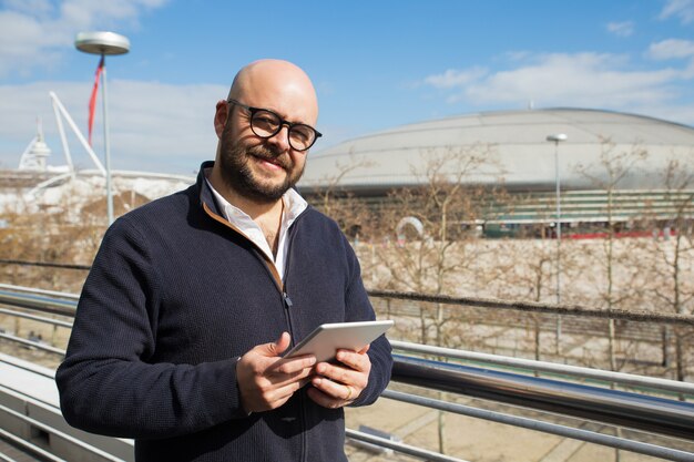 Hombre de mediana edad sonriente que usa la tableta al aire libre