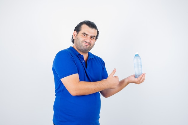 Hombre de mediana edad sosteniendo una botella de agua mientras muestra el pulgar hacia arriba en una camiseta de polo y parece satisfecho, vista frontal.