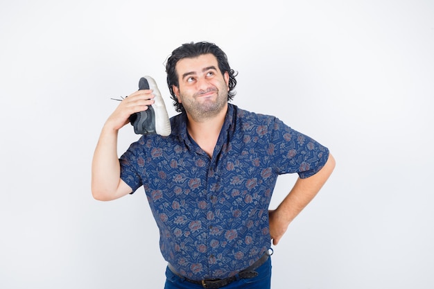 Hombre de mediana edad sosteniendo el zapato sobre el hombro en camisa y mirando pensativo, vista frontal.