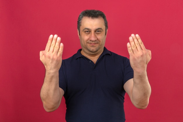 Hombre de mediana edad vistiendo polo que guía a alguien a la dirección de pie sobre la pared rosa aislado