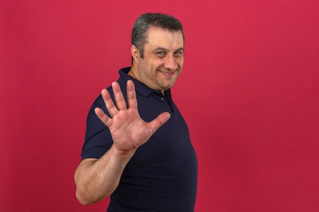 Hombre de mediana edad vistiendo polo con una sonrisa en la cara y mostrando el número cinco con los dedos sobre la pared rosa aislado