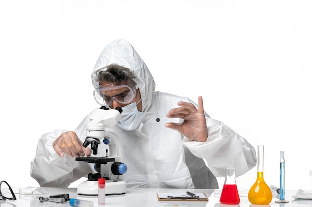 Hombre médico en traje de protección con máscara estéril con microscopio sobre blanco claro