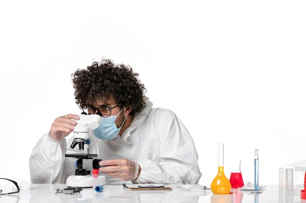 Hombre médico en traje de protección y máscara trabajando con microscopio en blanco