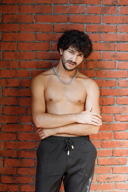 Hombre medio desnudo de pelo rizado posando para la cámara contra la pared.