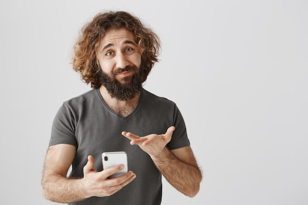 Hombre del Medio Oriente incierto mirando indeciso teléfono móvil, sintiéndose indeciso