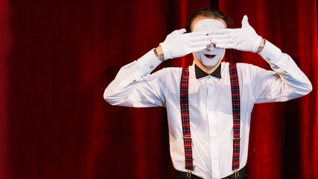 Hombre mime artista de pie delante de la cortina que cubre los ojos con las manos