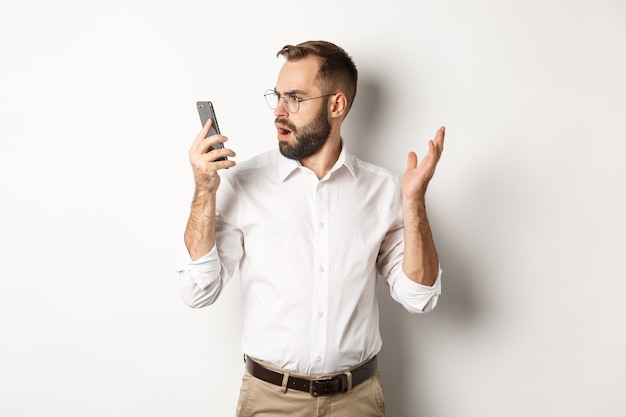 Hombre mirando confundido en el teléfono móvil después de la conversación, de pie perplejo Espacio de copia