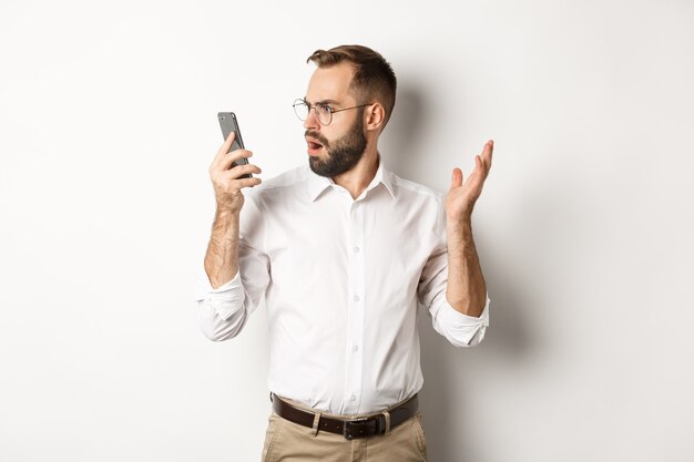 Hombre mirando confundido en el teléfono móvil después de la conversación, de pie perplejo Espacio de copia