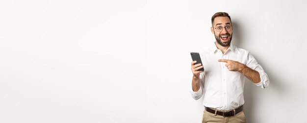 Hombre mirando emocionado y señalando con el dedo el teléfono móvil mostrando una buena oferta en línea de pie sobre Pentecostés