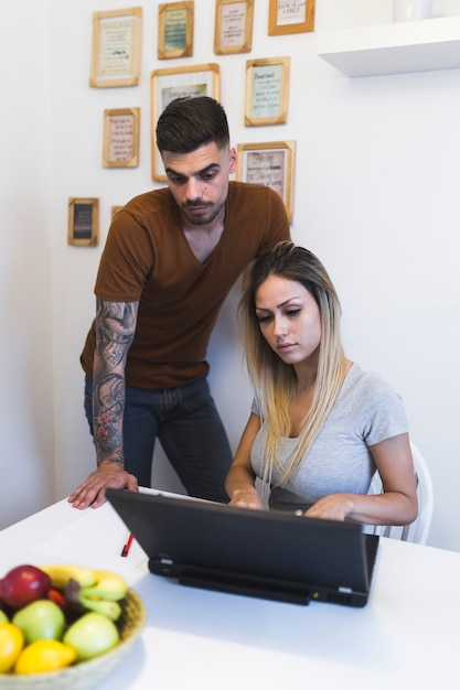 Hombre mirando a la mujer usando la computadora portátil en casa