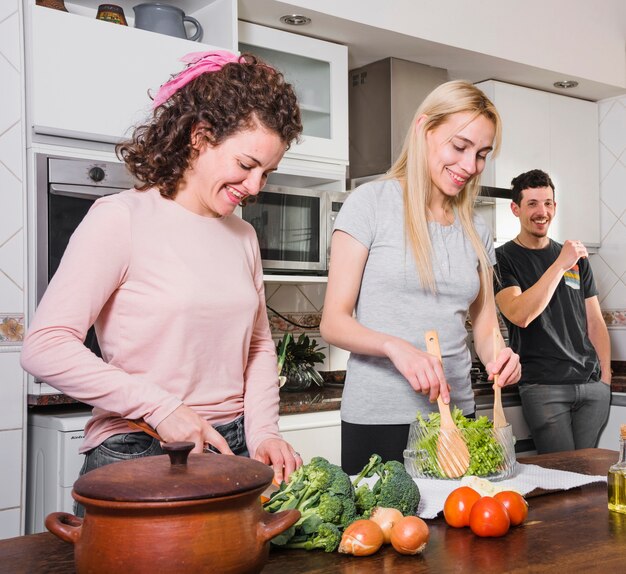 Hombre mirando a las mujeres jóvenes preparando ensalada en la mesa