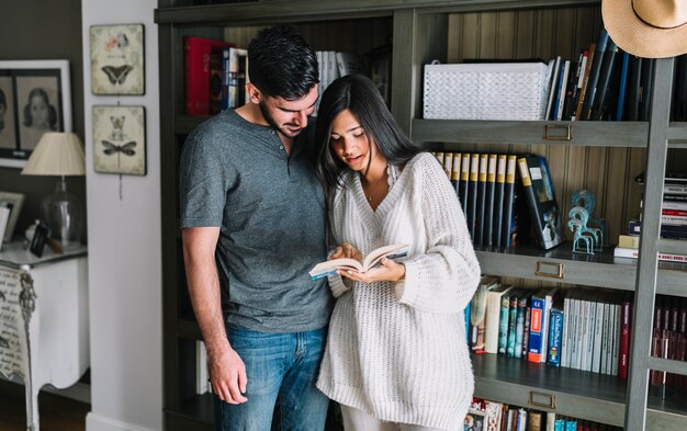 Hombre mirando a la novia leyendo el libro de pie delante de la estantería