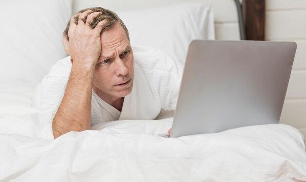 Hombre mirando preocupado en su computadora portátil en la cama