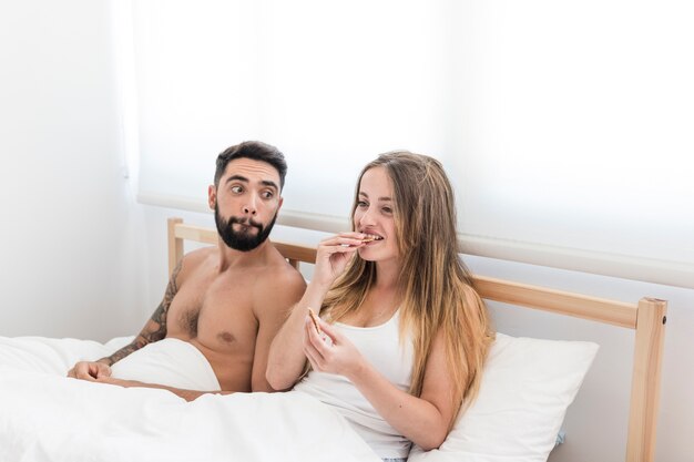 Hombre mirando a su esposa comiendo galletas en la cama