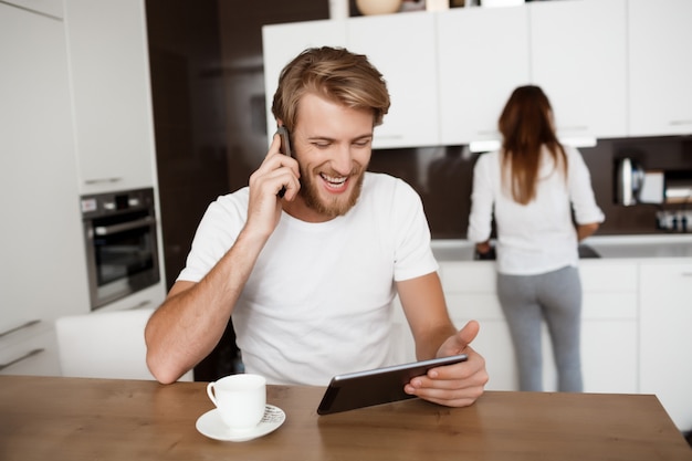 Hombre mirando tableta hablando por teléfono sonriendo. Novia