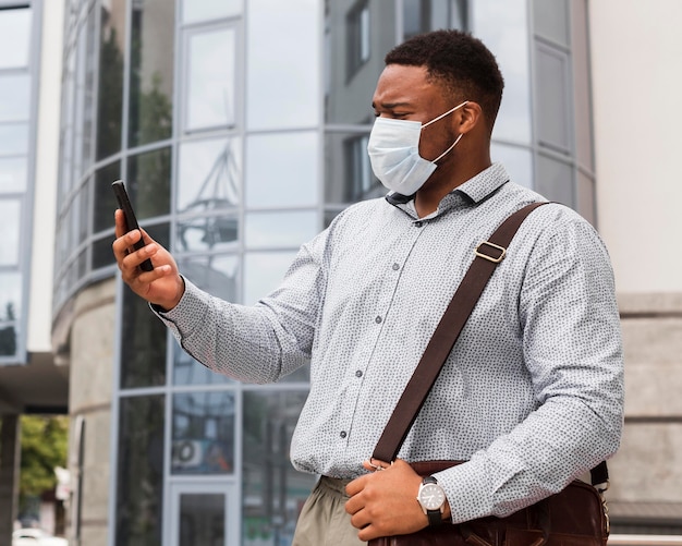 Hombre mirando el teléfono inteligente en su camino al trabajo mientras usa máscara