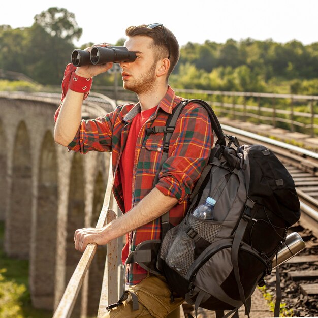 Hombre con mochila en puente mirando con binoculares