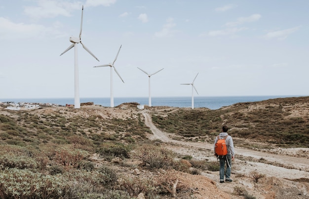 Un hombre con una mochila roja de pie y mirando los molinos de viento.