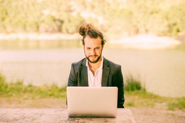 Hombre de moda que trabaja con el ordenador portátil al aire libre