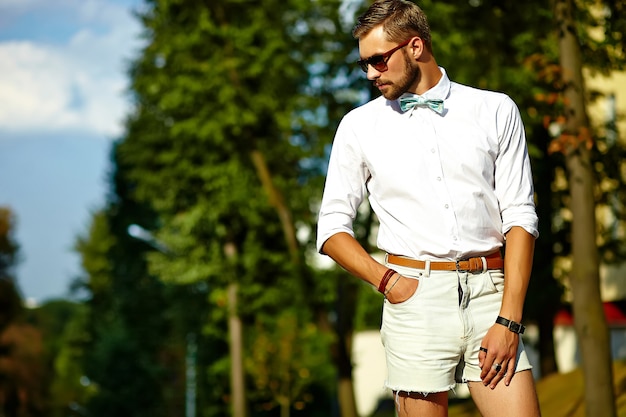 Hombre modelo guapo hipster en ropa de verano elegante posando en gafas de sol