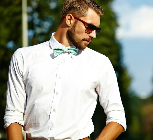 Hombre modelo guapo hipster en ropa de verano elegante posando en gafas de sol