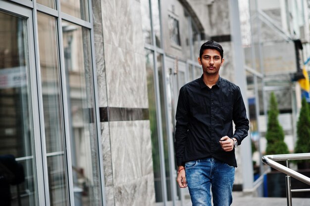 Hombre modelo indio con estilo en ropa casual camisa negra posada al aire libre en la calle de la India