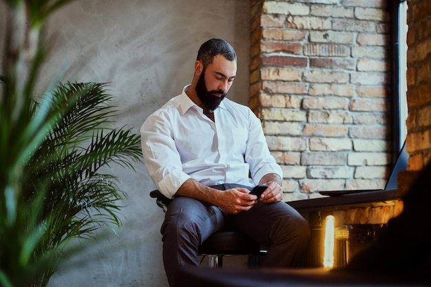 Hombre moderno barbudo usando un smartphone en una habitación con interior tipo loft.