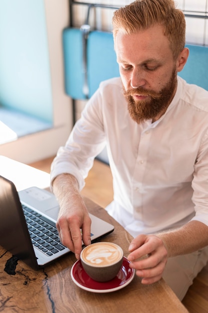 Hombre moderno colocando su taza de café junto a su computadora portátil