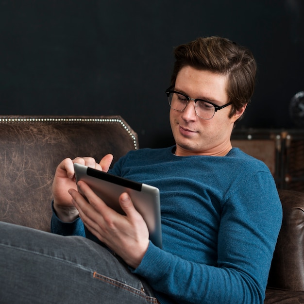 Hombre moderno mirando en su tableta mientras permanece en su sofá