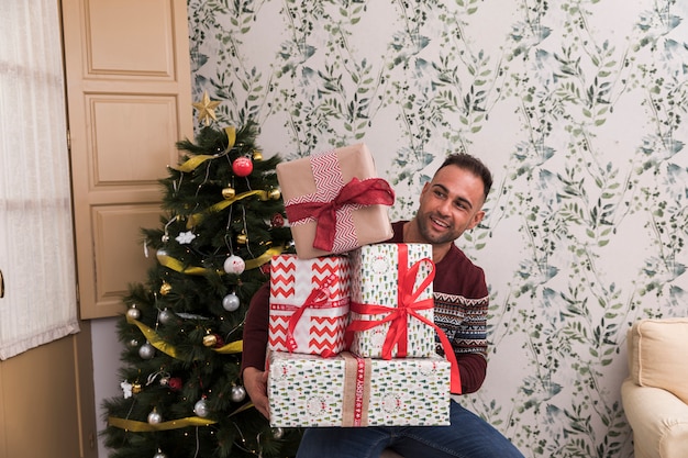 Hombre con montón de regalos cerca del árbol de navidad