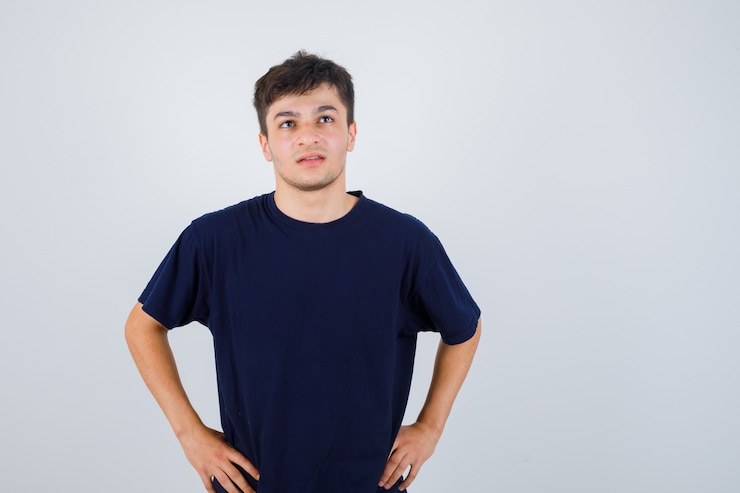 Foto gratuito hombre morena posando con las manos en la cintura en camiseta y mirando pensativo, vista frontal.