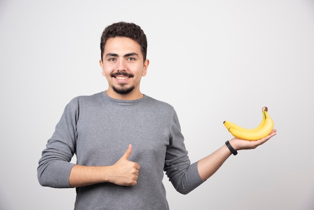 Hombre morena sosteniendo plátano y dando pulgares.