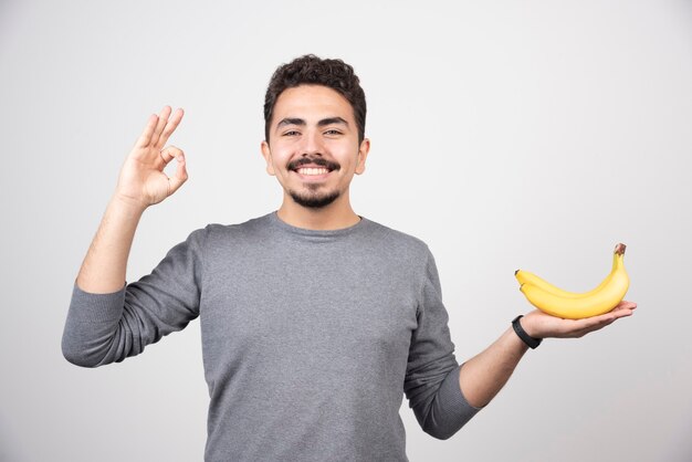 Hombre morena sosteniendo plátano y dando señal ok.