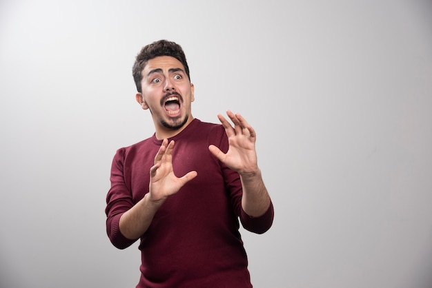 Un hombre moreno asustado sobre una pared gris.