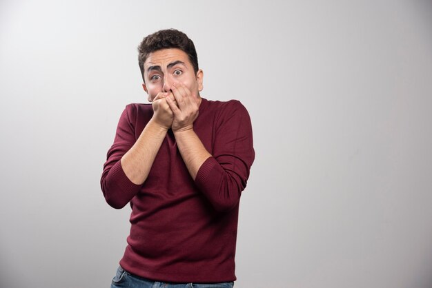 Un hombre moreno asustado sobre una pared gris.