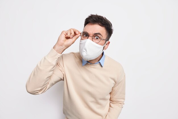 El hombre moreno atento y serio usa una máscara protectora en un lugar público mantiene la mano en las gafas se previene del coronavirus vestido de manera informal