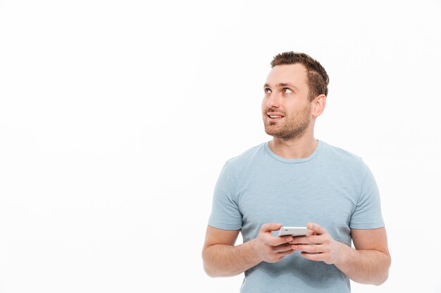 Hombre moreno positivo que tiene cerdas sonriendo y mirando a un lado mientras usa el espacio de copia del teléfono inteligente