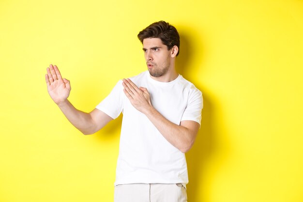 Hombre mostrando habilidades de kung-fu, movimiento ninja de artes marciales, de pie con camiseta blanca listo para luchar, de pie sobre fondo amarillo