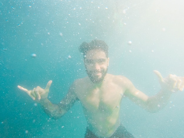 Foto gratuita hombre mostrando signo de mano shaka bajo el agua