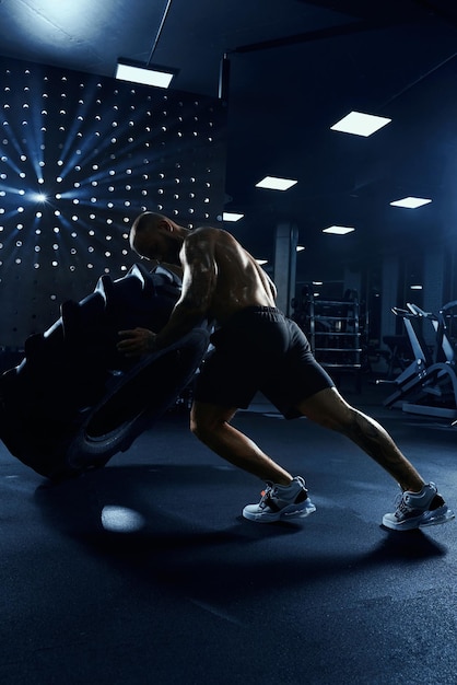 Foto gratuita hombre moviendo rueda de neumático gigante en el gimnasio