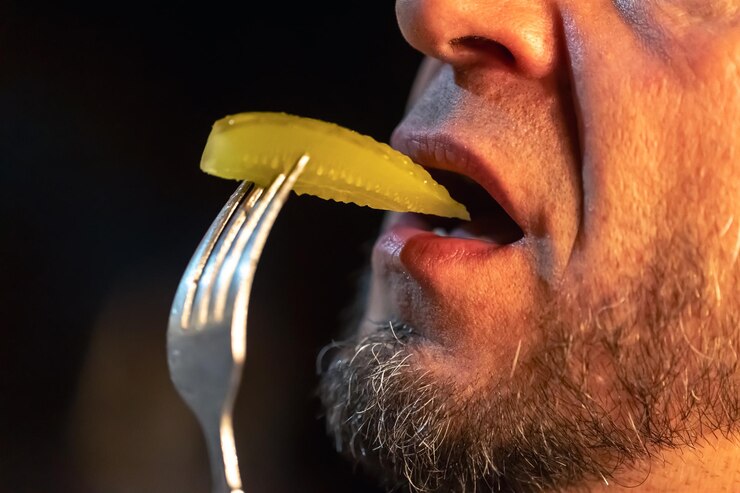 Foto gratuito un hombre muerde un trozo de pepino ligeramente salado pinchado con un tenedor