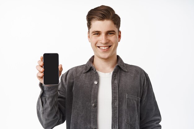 El hombre muestra la pantalla del teléfono inteligente, la interfaz de la aplicación, la aplicación recomendada, de pie en blanco