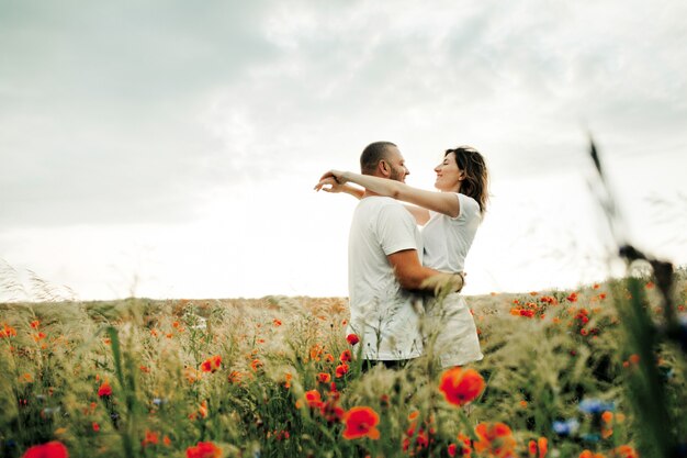 Hombre y mujer se abrazan de pie entre el hermoso campo de amapolas