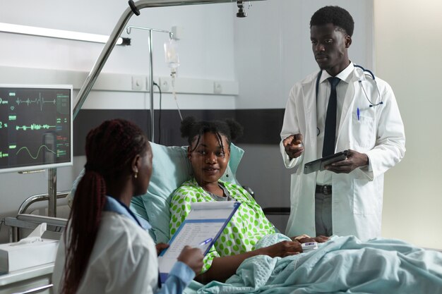 Hombre y mujer afroamericanos hablando con una niña en la sala del hospital sobre el tratamiento y el diagnóstico de curación. Los médicos que examinan a un paciente joven enfermo con collarín cervical sentado en la cama