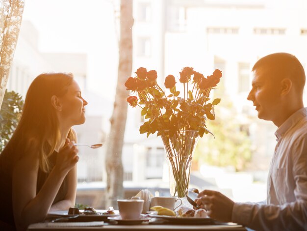 Hombre y mujer atractiva en mesa con postres y flores.