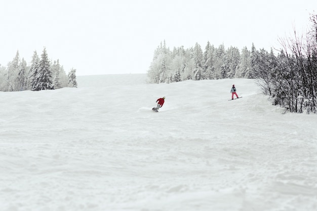 El hombre y la mujer bajan la colina en las tablas de snowboard